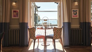 Comedor con una mesa preparada para cuatro personas, vista al mar y un servicio de té de tres niveles.