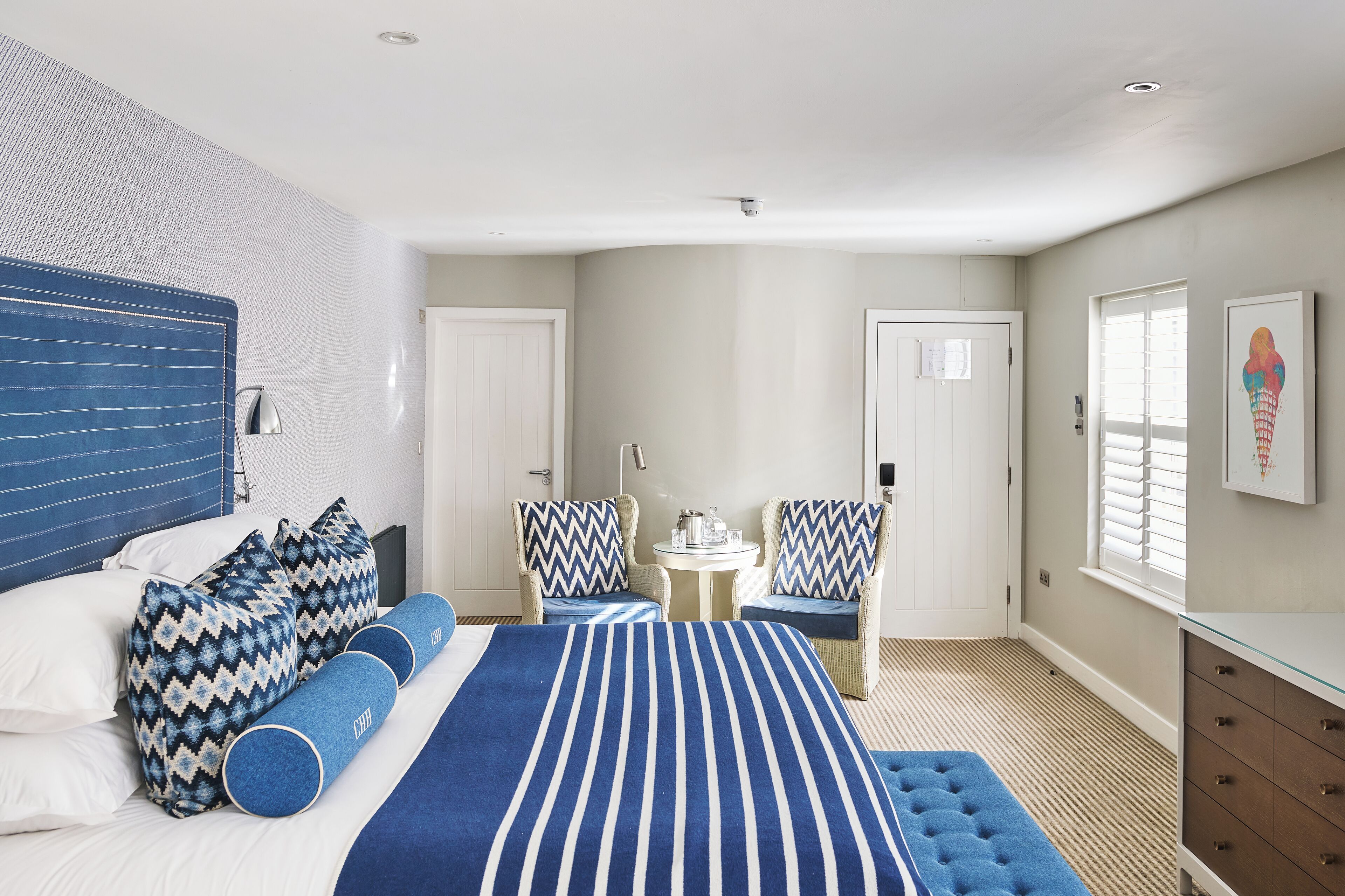 A bedroom with a bed, two chairs, a small table, and a dresser.