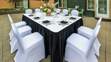 Un ensemble de mobilier de jardin comprenant une table à manger rectangulaire, des chaises blanches, une nappe noire et un vase rempli de fleurs.