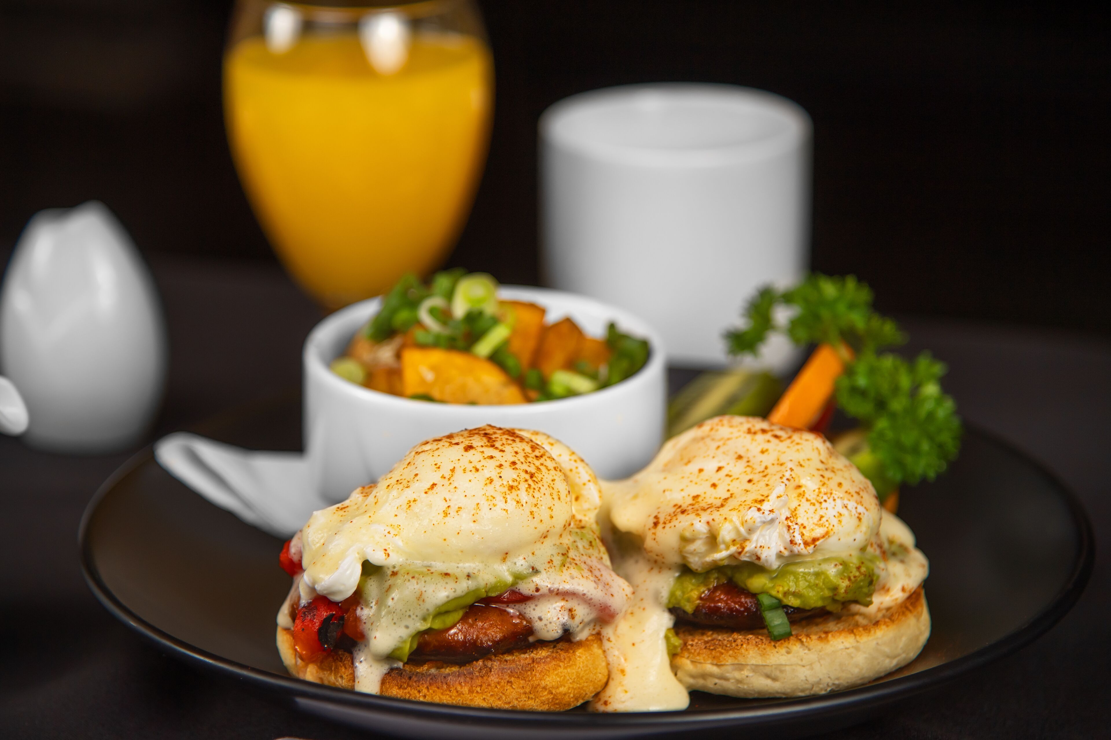 A breakfast plate with eggs benedict, a side salad, and a glass of orange juice.