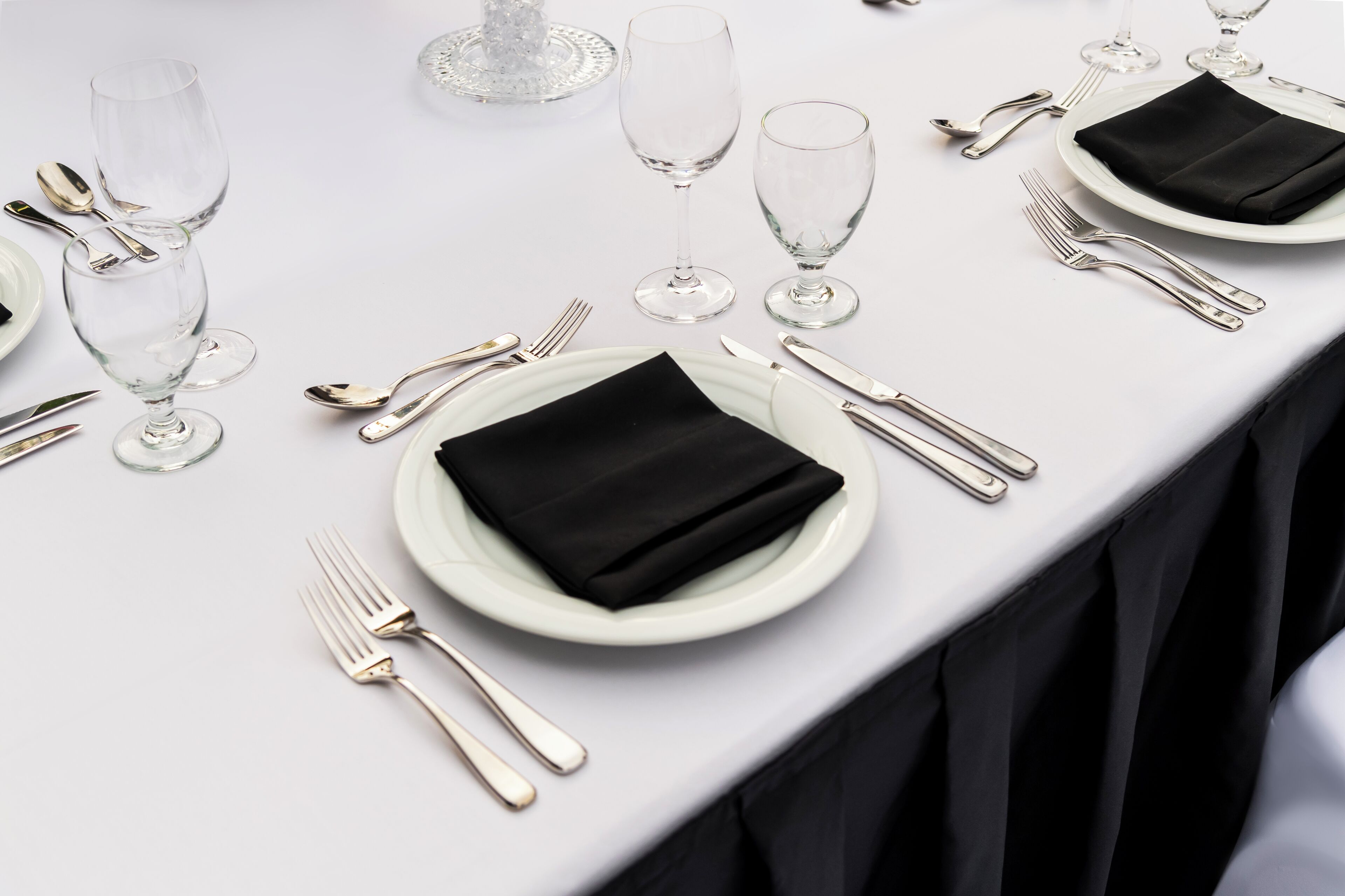 Een gedekte tafel met witte borden, zwarte servetten en bestek.