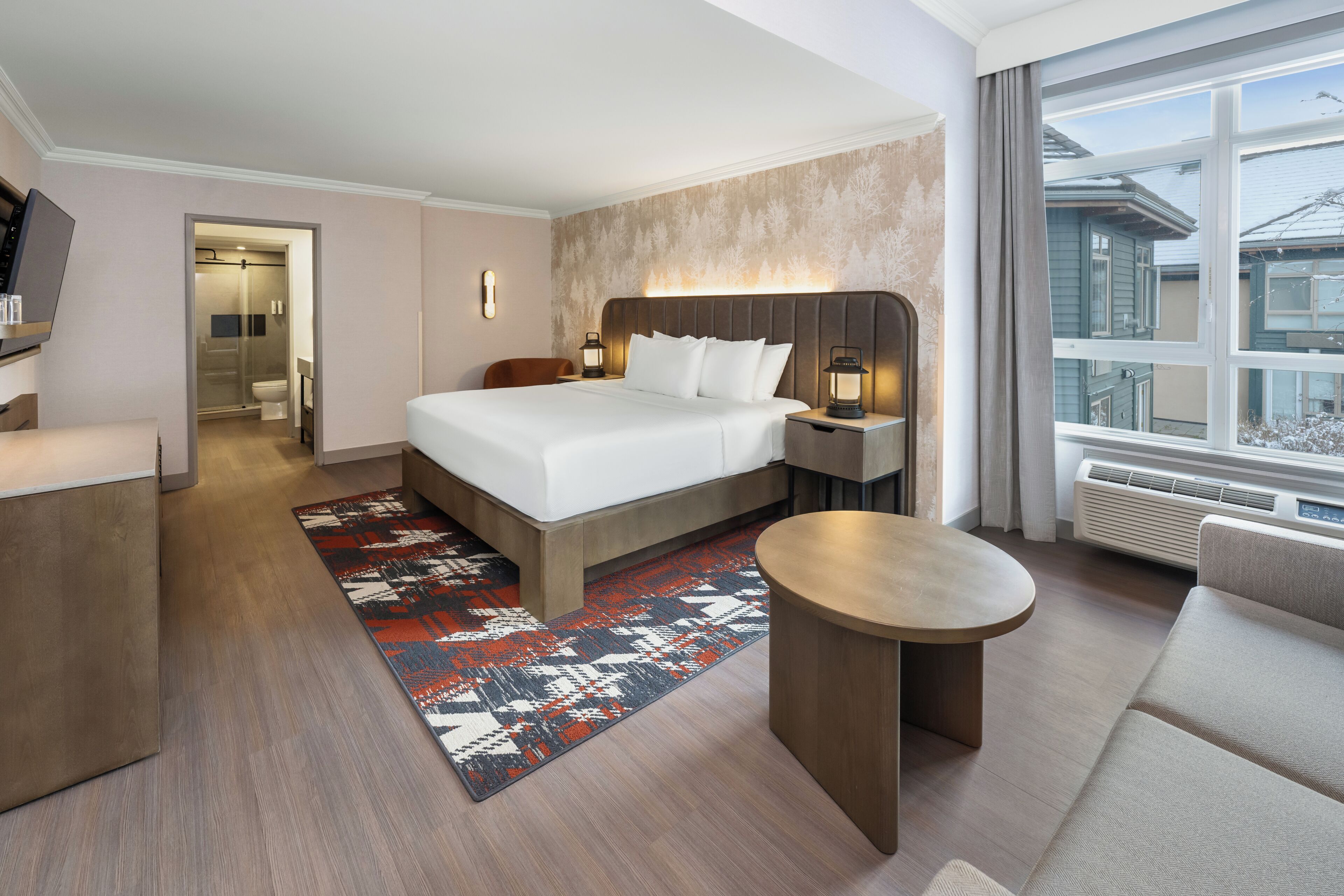 Une chambre d’hôtel avec un lit, une table de chevet, une lampe et une vue sur l’extérieur.