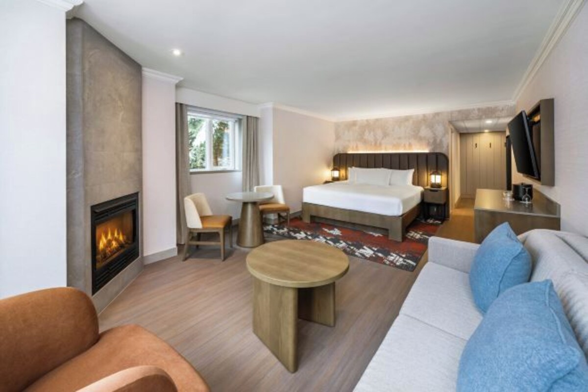 A hotel room with a bed, a TV, a fireplace, a sofa, a coffee table, and a dining area.