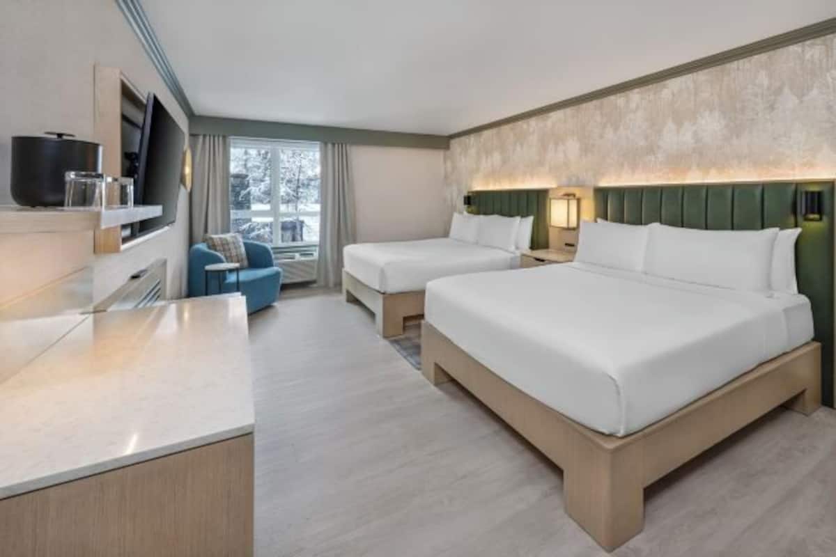 Une chambre dâhĂŽtel avec deux lits, une tĂ©lĂ©vision, un bureau et une vue sur lâextĂ©rieur.