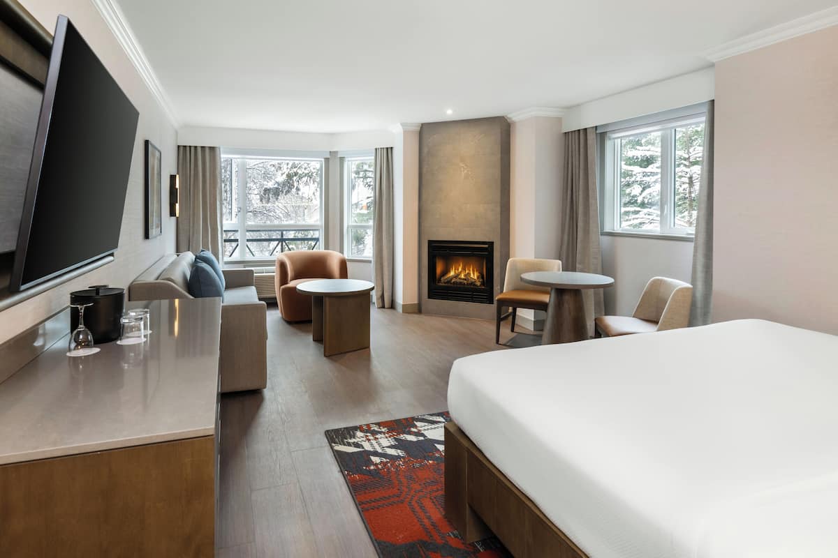Une chambre dâhĂŽtel comprenant un lit, une tĂ©lĂ©vision, une cheminĂ©e, un canapĂ©, un fauteuil et une petite table.