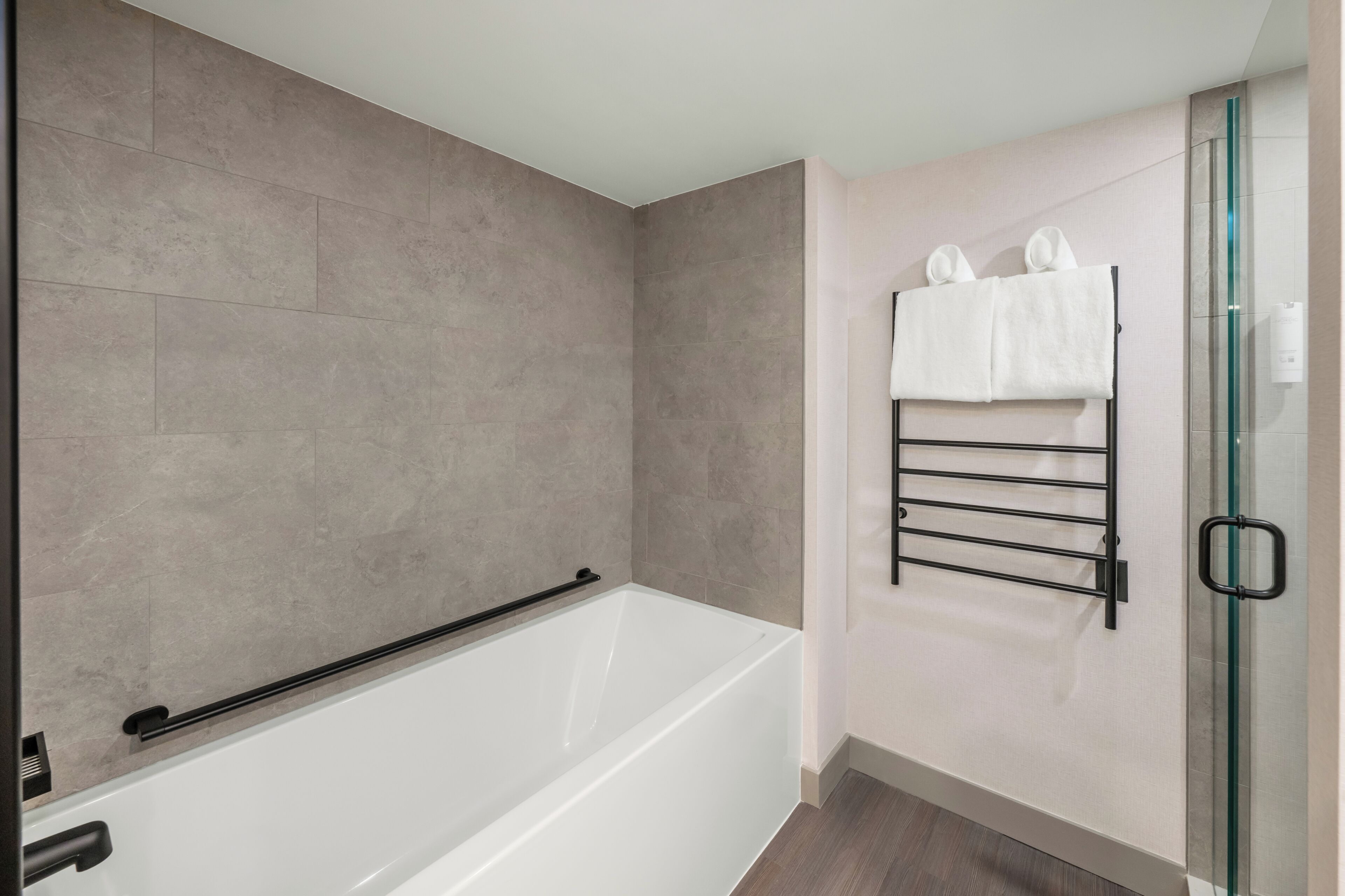 A modern bathroom with a bathtub, a glass shower enclosure, and a towel rack with towels.