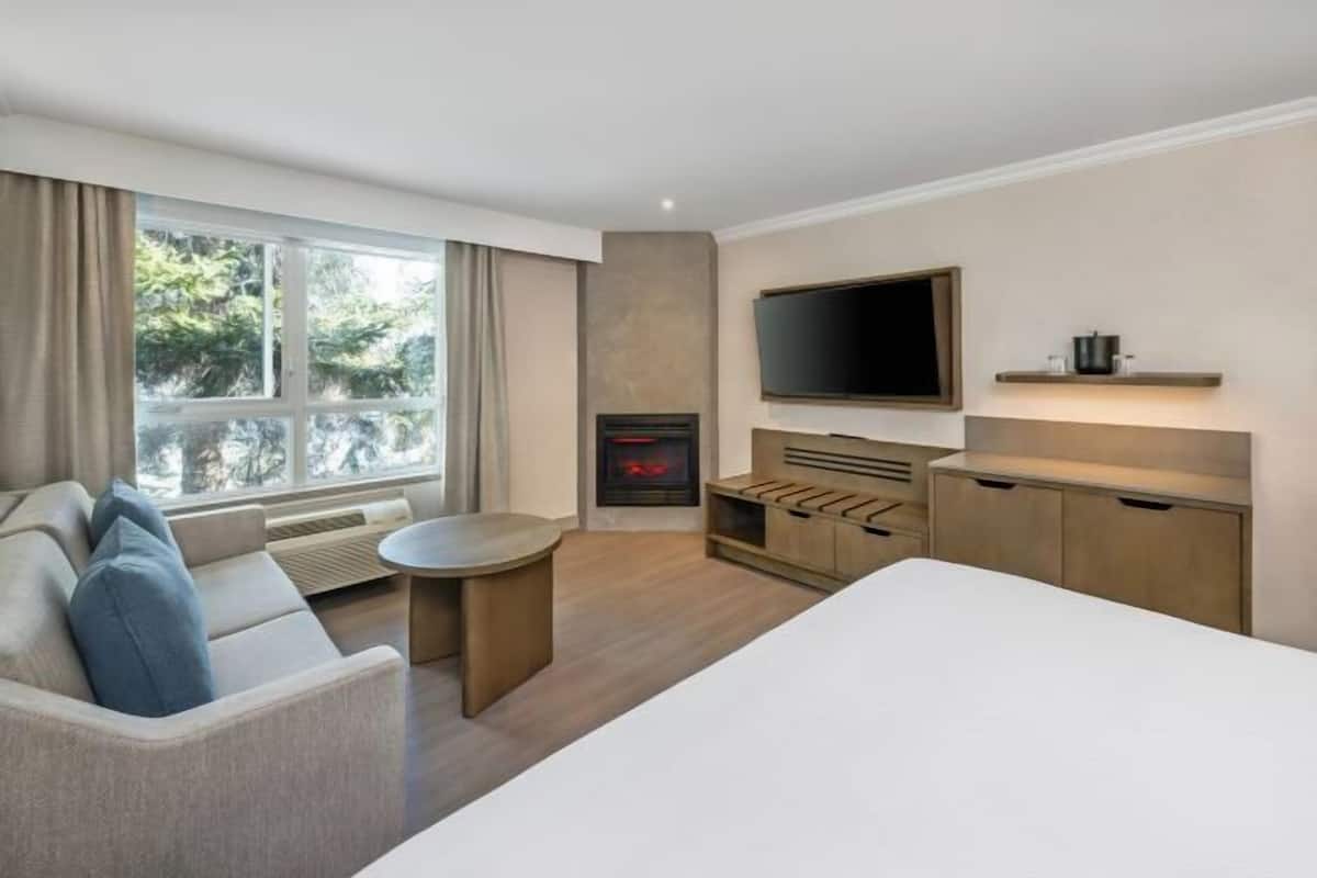 A modern hotel room with a sofa, a bed, a TV, a fireplace, and a dining area.