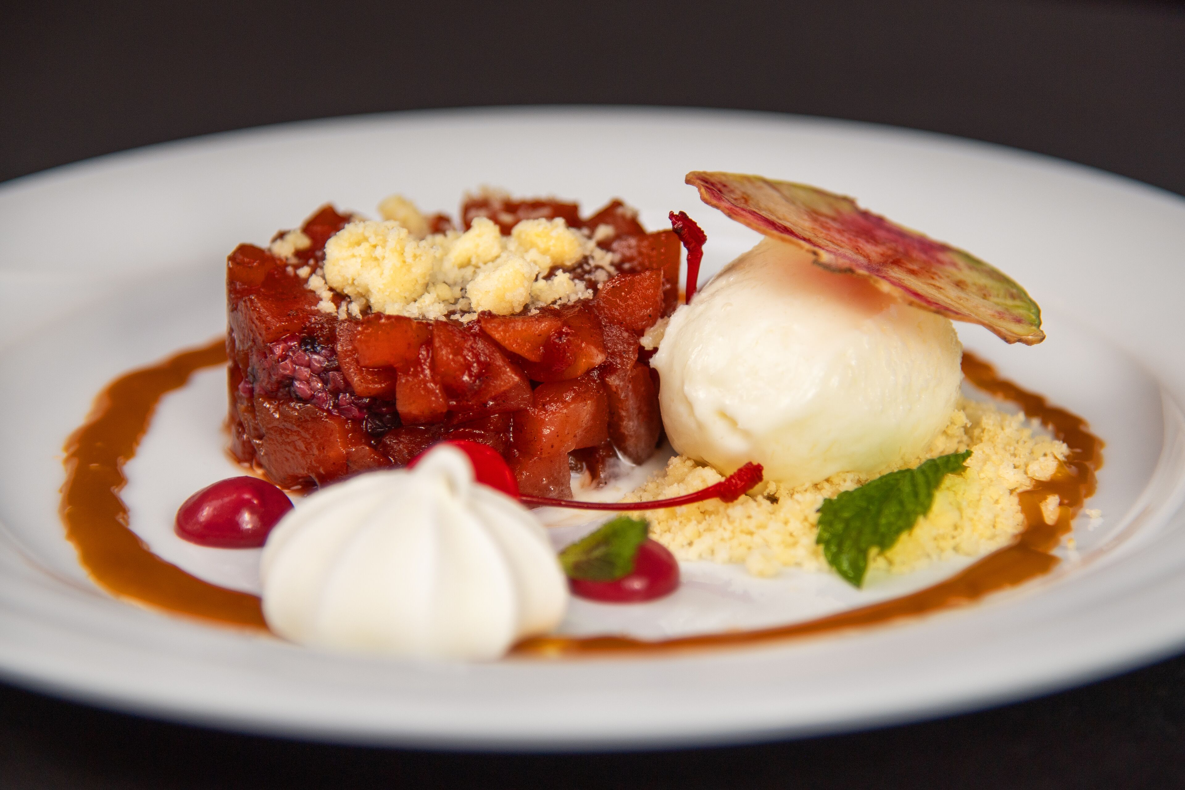 Une assiette à dessert comprenant une portion de fruits caramélisés, une boule de glace et une feuille de menthe en guise de décoration.