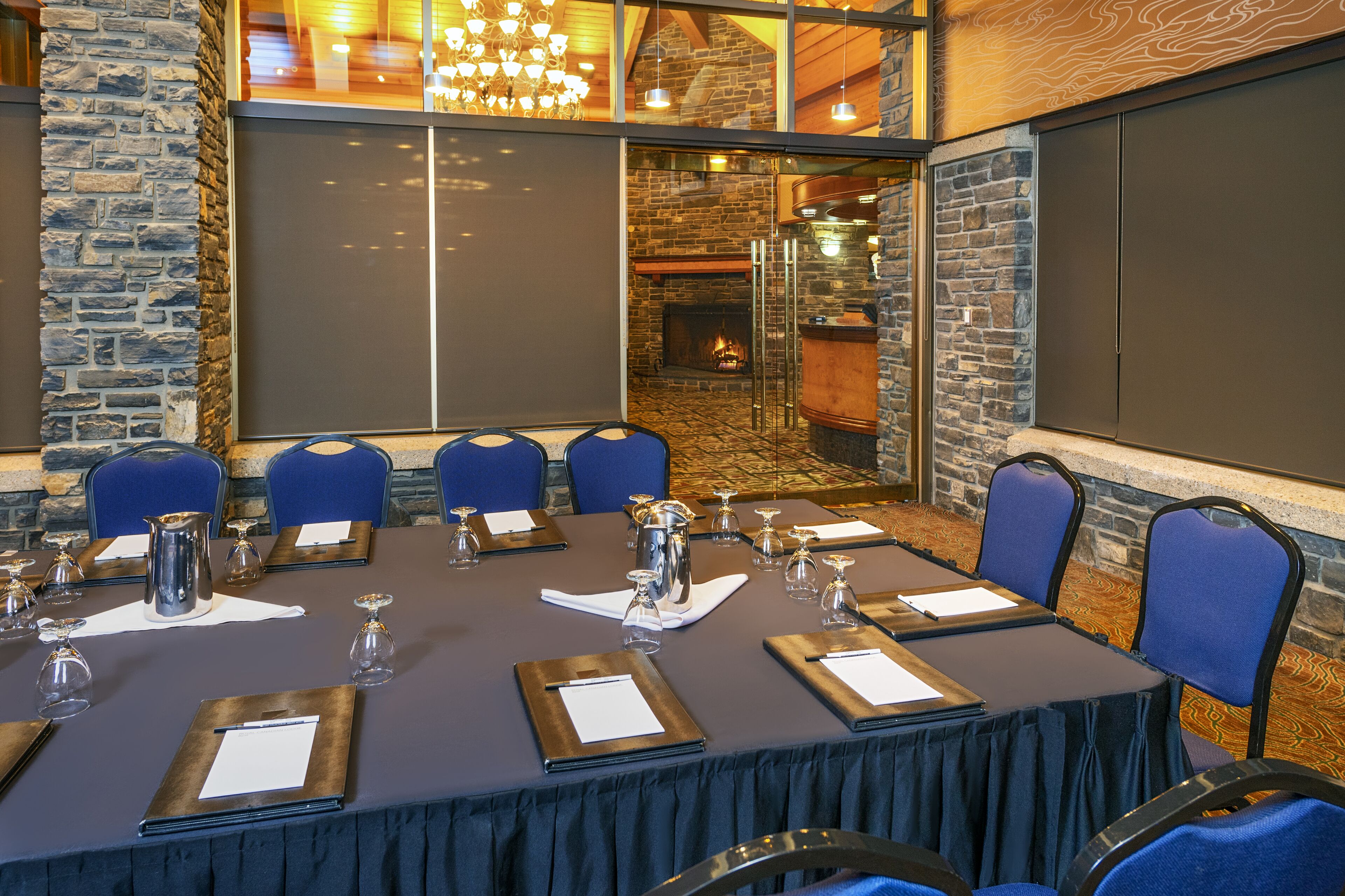 Un salón de conferencias con una larga mesa, sillas azules y una chimenea al fondo.