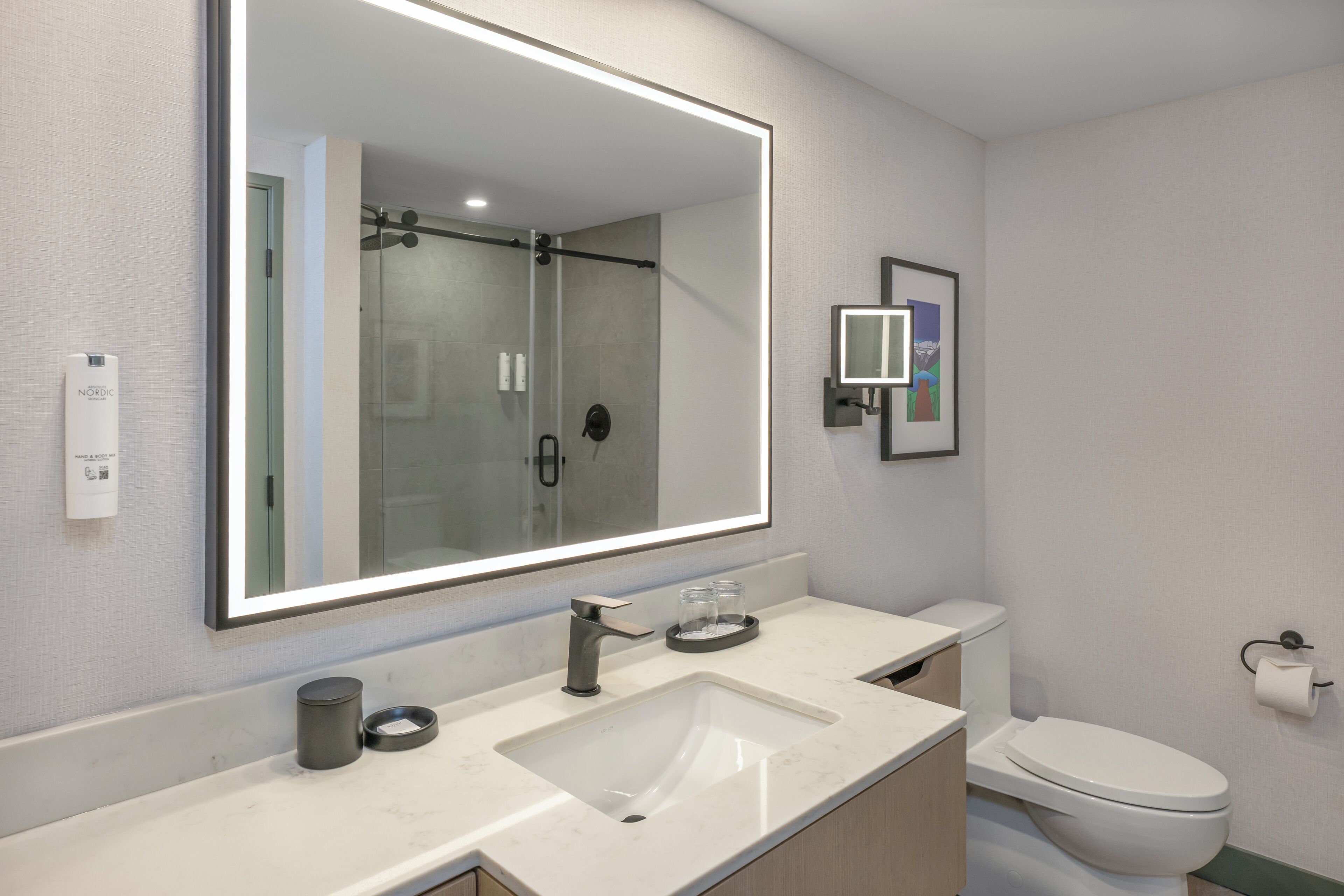 Une salle de bain moderne avec un grand miroir, un lavabo, des toilettes et un espace douche.