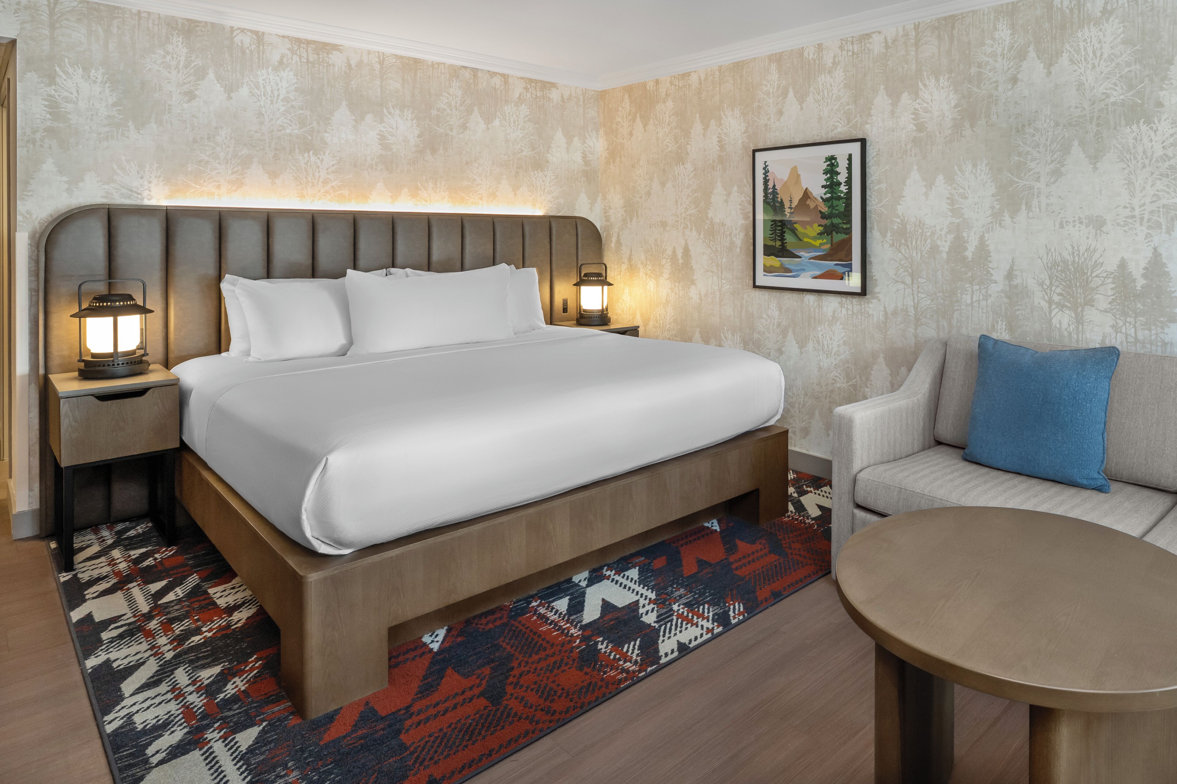 Una habitación de hotel con una cama grande, un sofá, una mesita y una mesita de noche con una lámpara.