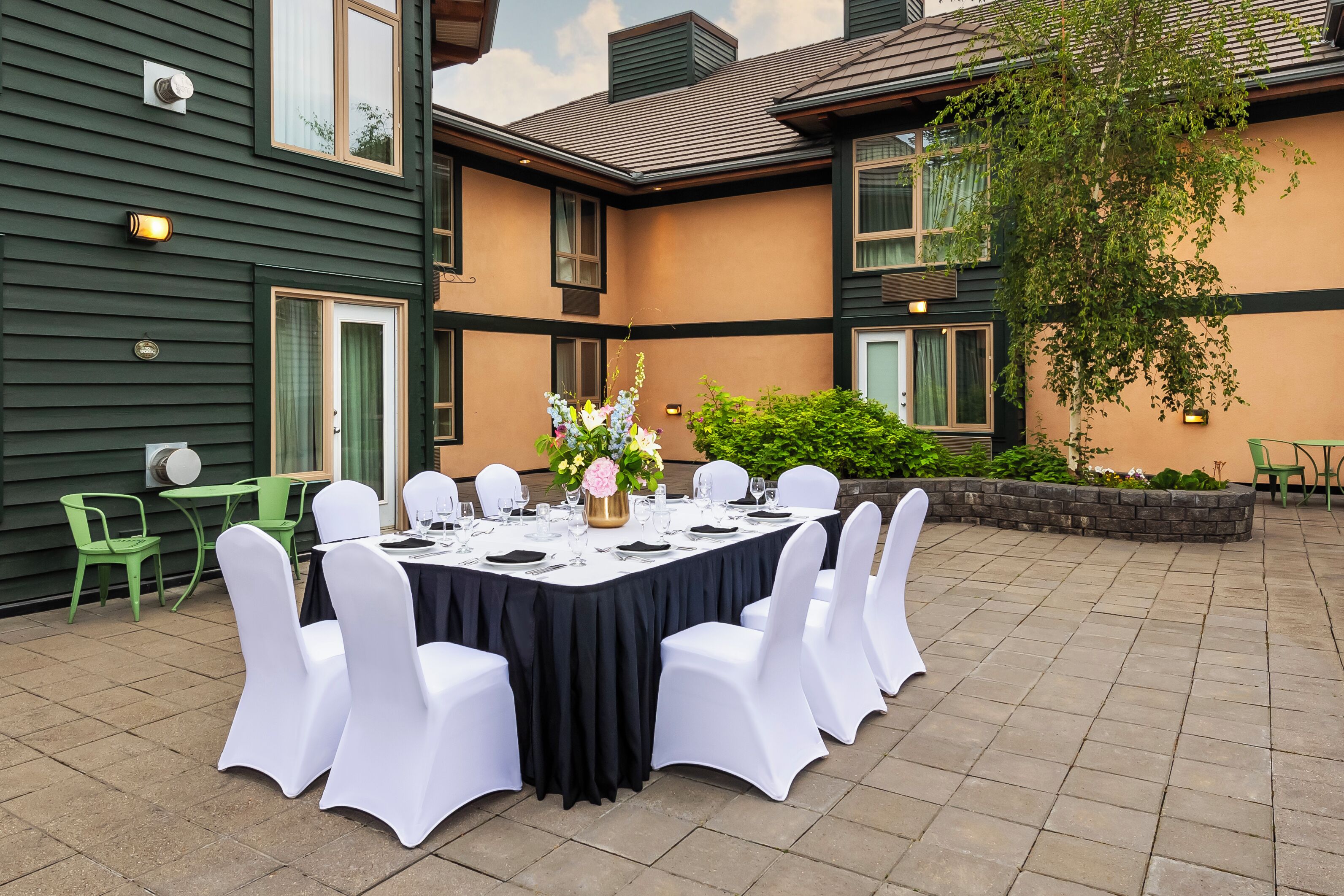 An outdoor dining area with a round table set for six, surrounded by white chairs.