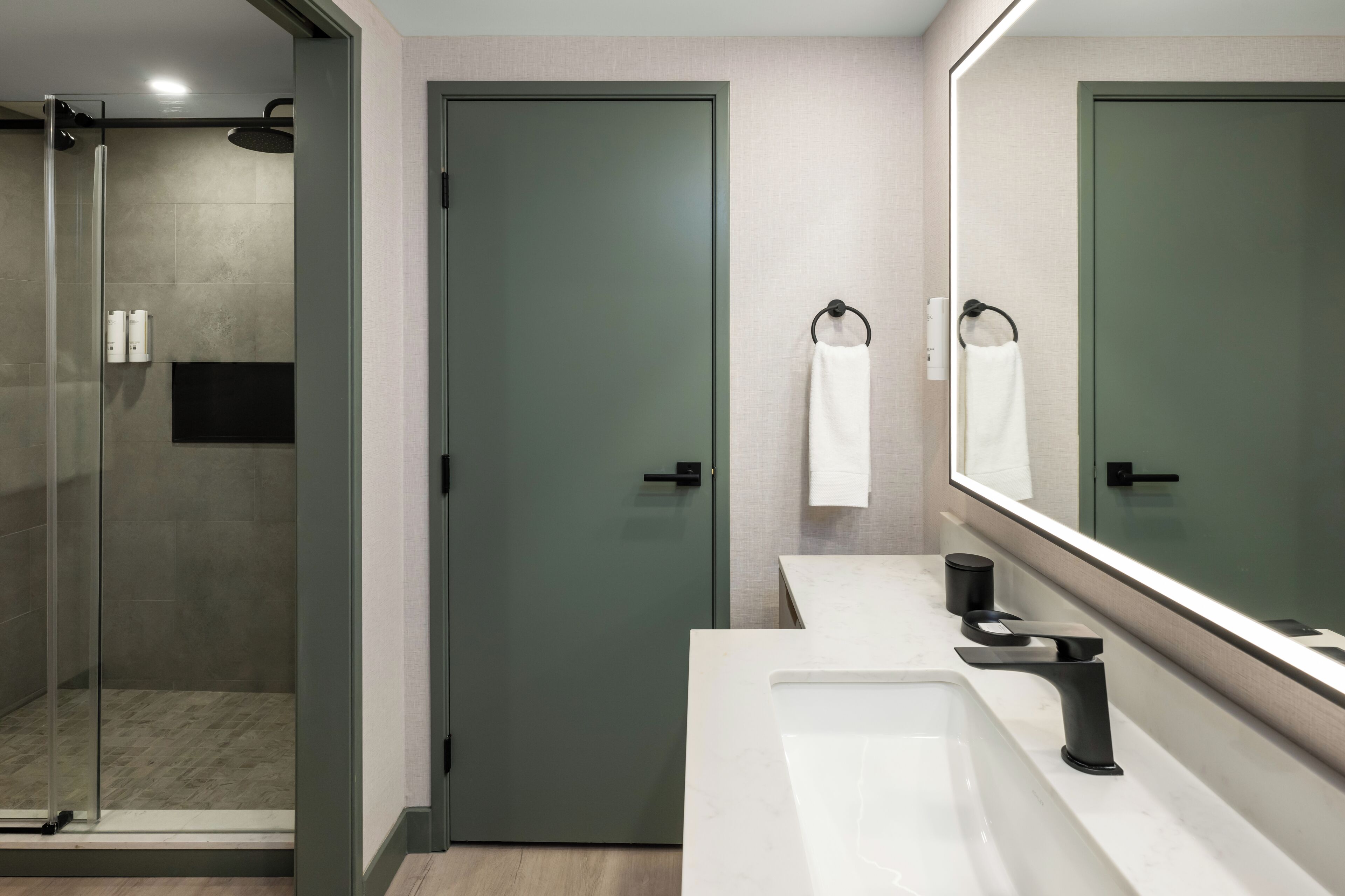 Une salle de bain moderne avec une douche à parois de verre, un lavabo blanc doté d’un robinet noir et un grand miroir au-dessus du lavabo.