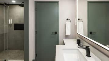 Une salle de bain moderne avec une douche à parois de verre, un lavabo blanc doté d’un robinet noir et un grand miroir au-dessus du lavabo.