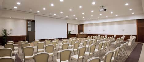 A conference room with rows of chairs, a podium, and a projector screen.