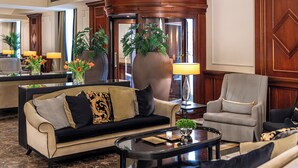 A well-furnished lobby with a sofa, armchair, and coffee table, featuring a large vase with plants and a mirror reflecting the room. - Starhotels Majestic (Turin)