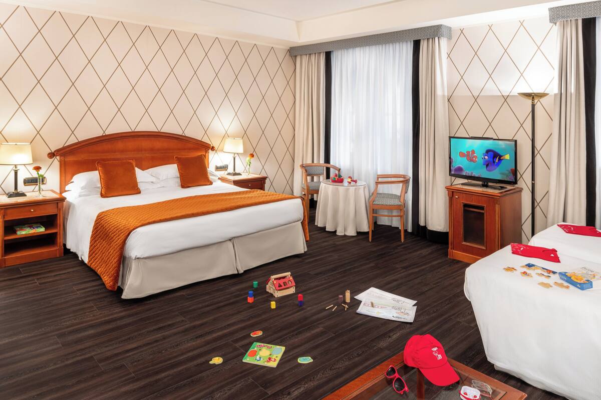 A hotel room with a large bed, a TV, a desk with a chair, and a small table.