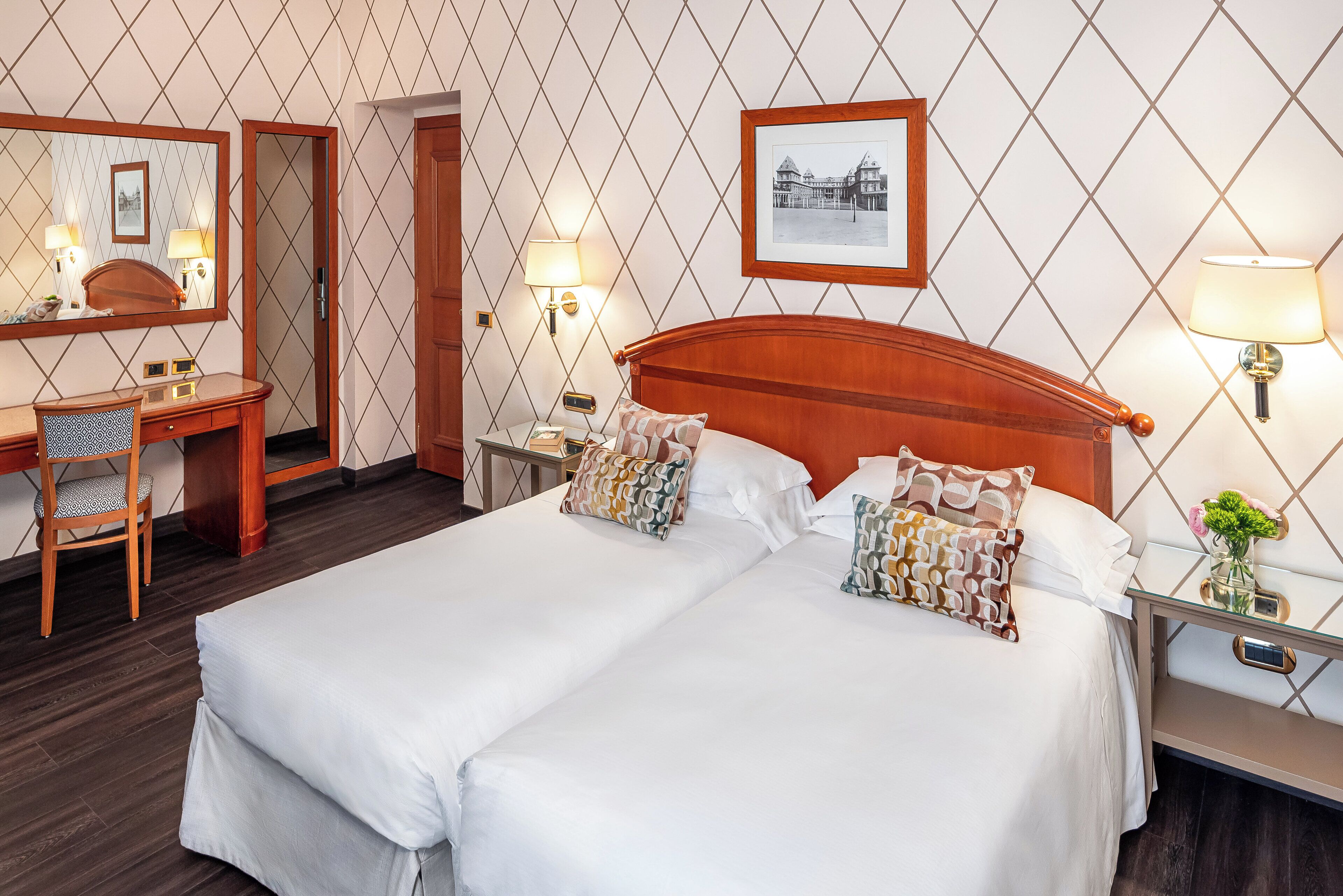 Une chambre d’hôtel avec un grand lit, un bureau avec une chaise, une table de chevet avec une lampe et un tableau encadré au mur.