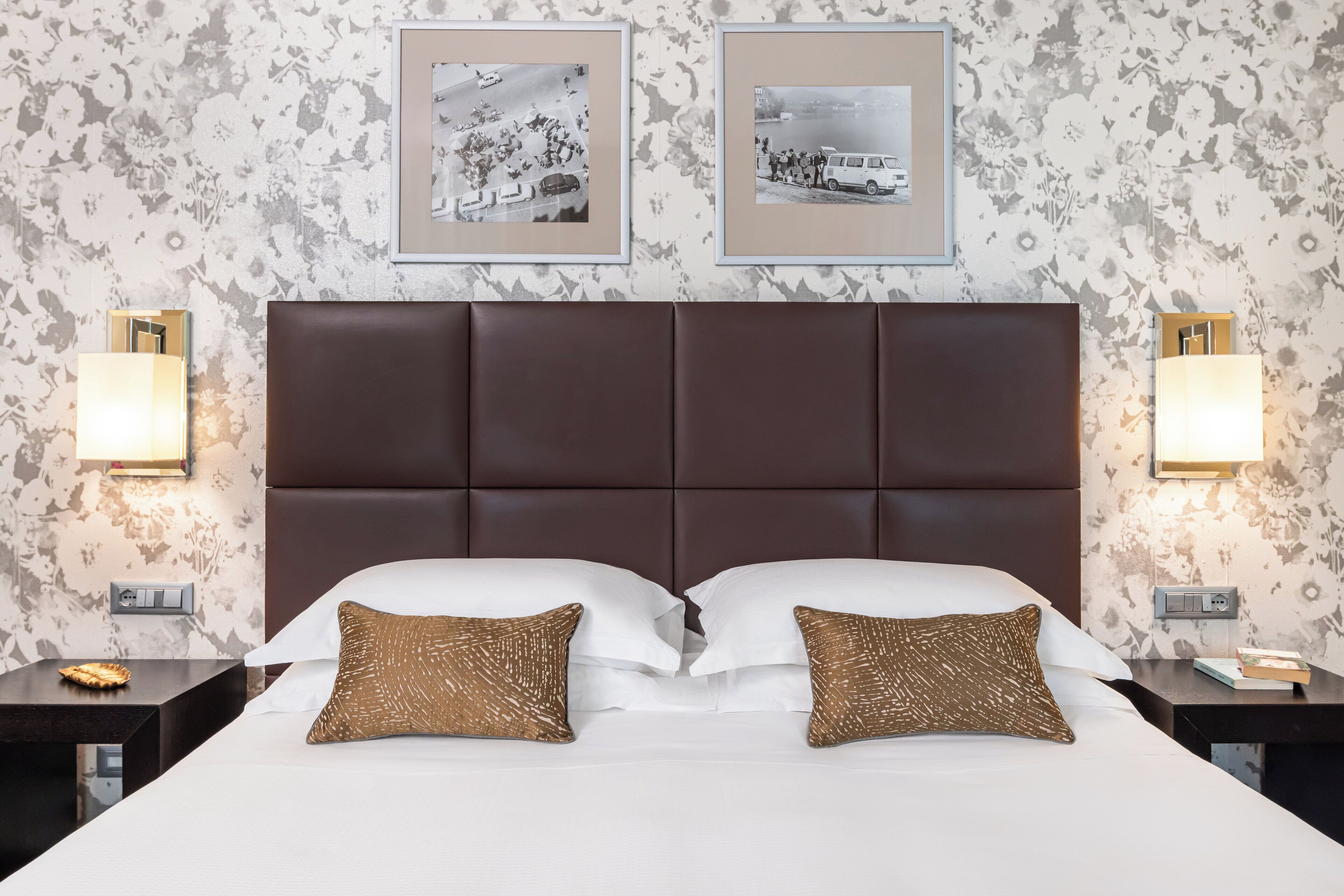 Habitación de hotel con una cama grande, dos almohadas, cabecera y cuadros en la pared.