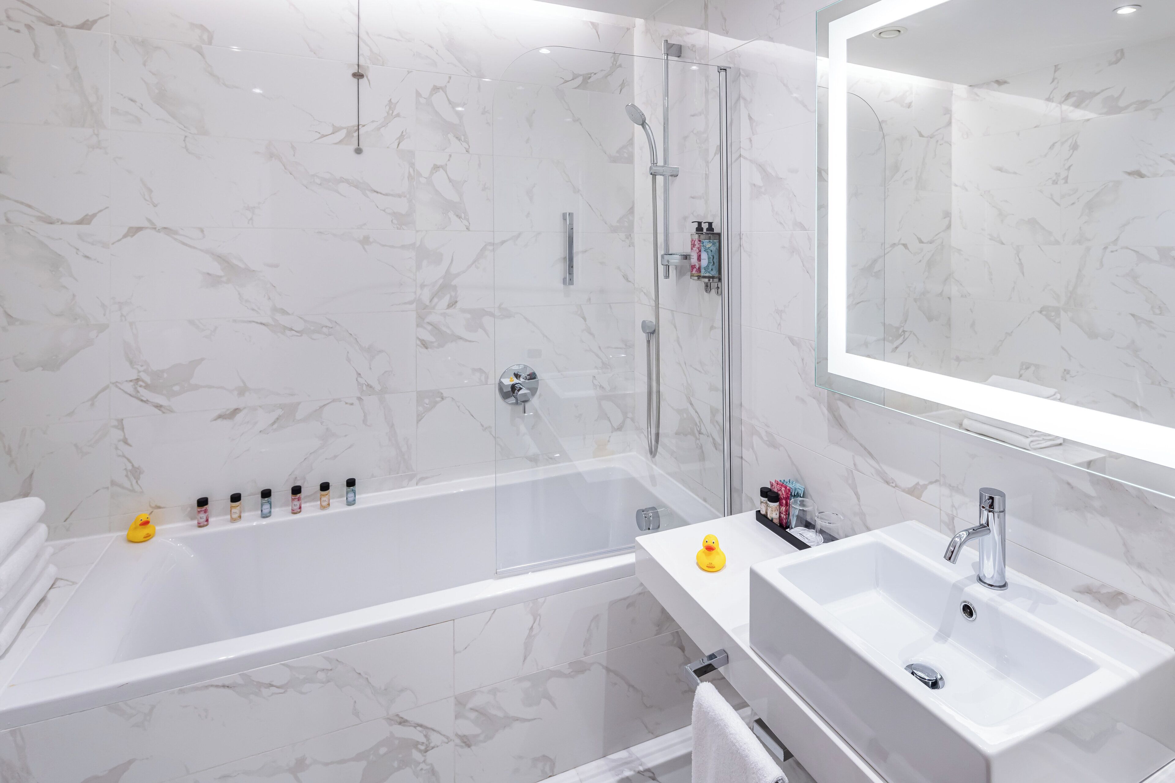 Un bagno moderno con parete in marmo, cabina doccia in vetro, vasca da bagno bianca e lavabo con specchio soprastante.