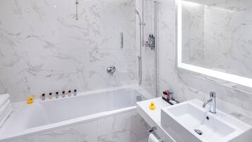 Un bagno moderno con parete in marmo, cabina doccia in vetro, vasca da bagno bianca e lavabo con specchio soprastante.