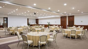 Un salón de conferencias con varias mesas redondas, cada una rodeada de sillas, y equipada con tarjetas de identificación y botellas de agua.