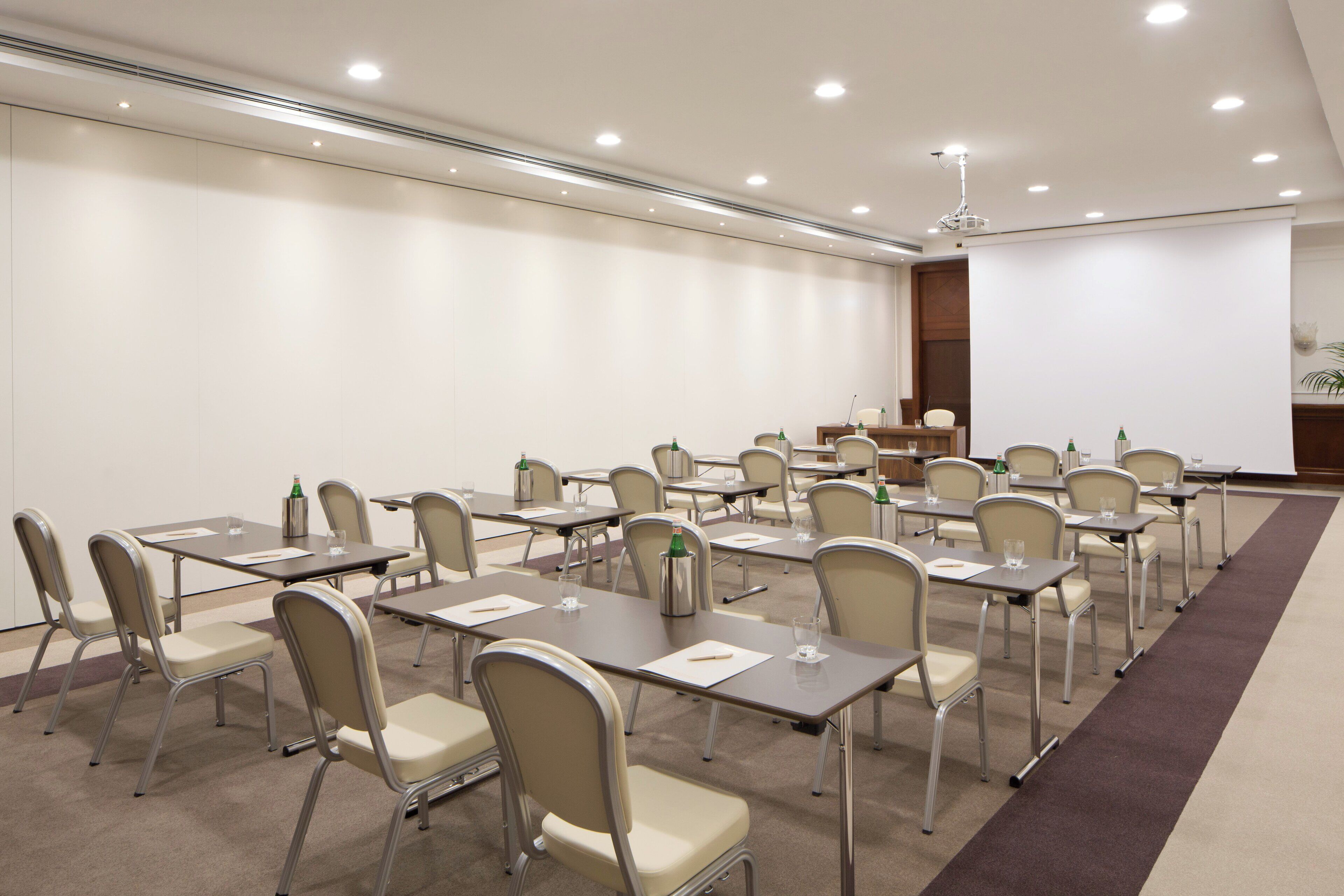 Une salle de conférence avec des rangées de tables et de chaises, équipée de bouteilles d’eau et de blocs-notes.