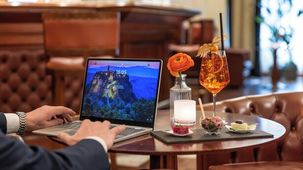 A laptop on a table with a dessert and a drink, a candle, and a vase with a flower. - Starhotels Majestic (Turin)
