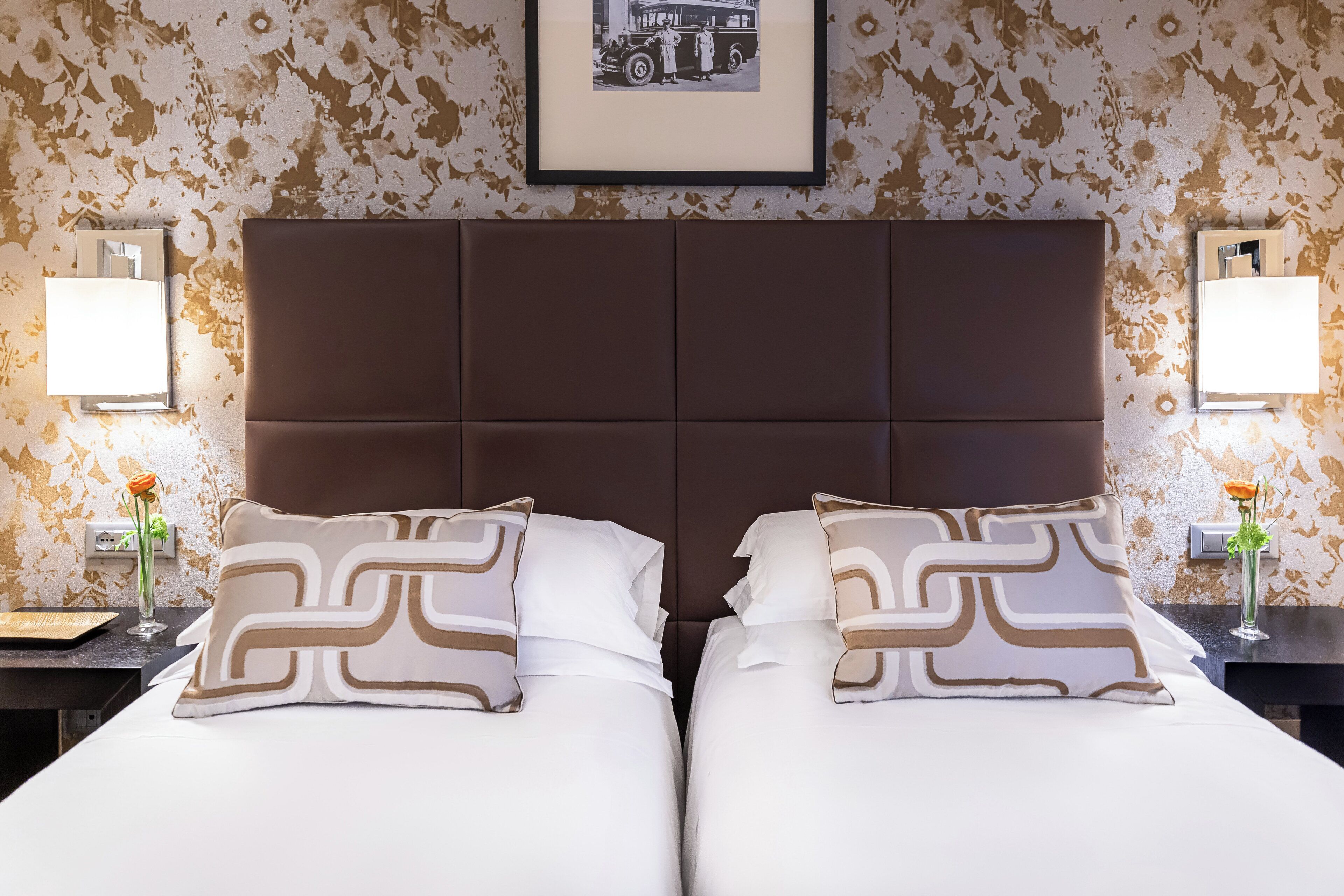A double bed with a brown headboard, two bedside tables with lamps, and a framed picture on the wall.