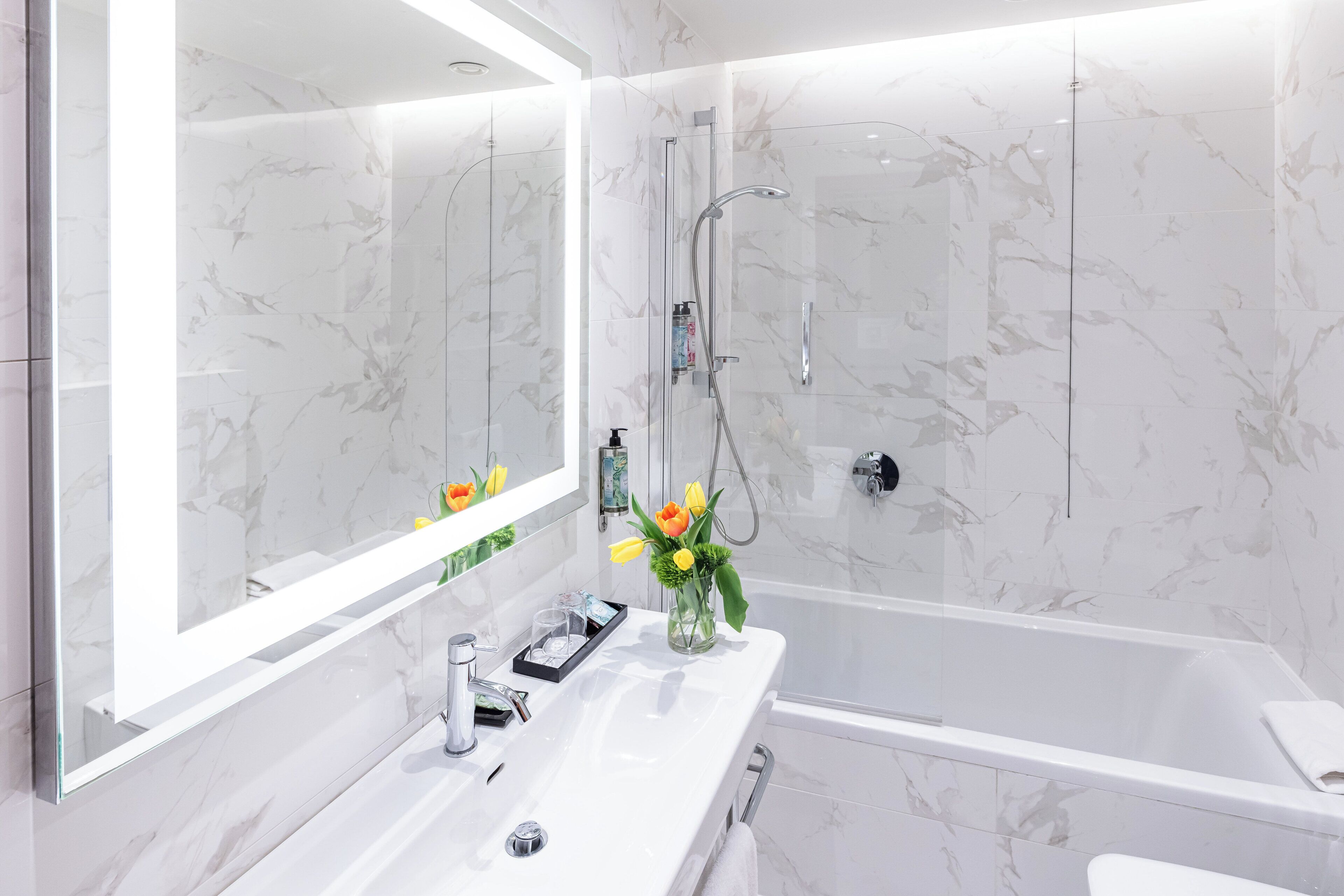 Un baño moderno con un espejo grande, un lavamanos blanco, una bañera y una zona de ducha.