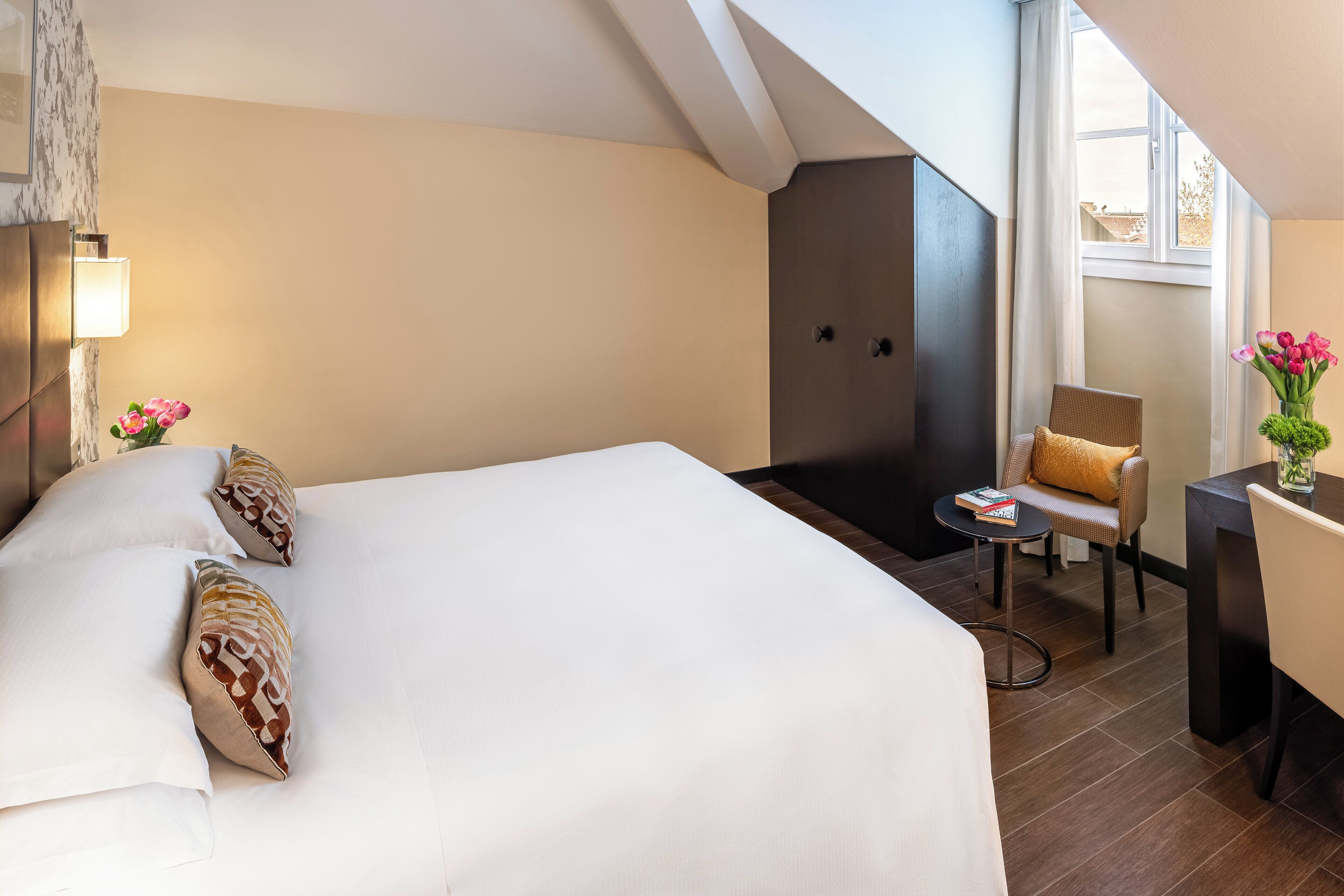 Une chambre d’hôtel avec un grand lit, une petite table avec une chaise, un bureau avec une chaise et une fenêtre avec des rideaux.