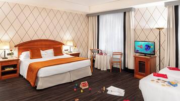 A hotel room with a large bed, a TV, a desk with a chair, and a small table.