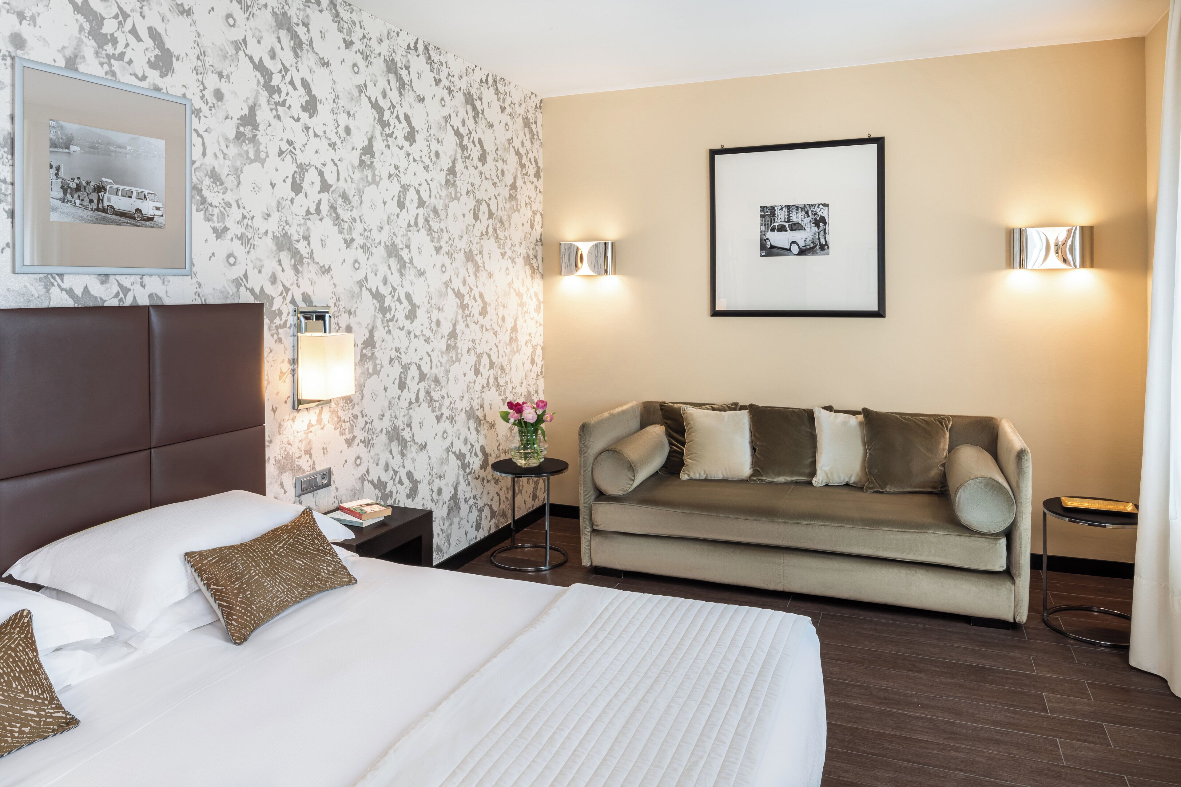 Habitación de hotel con una cama grande, un sofá, dos lámparas fijadas a la pared y un cuadro enmarcado.
