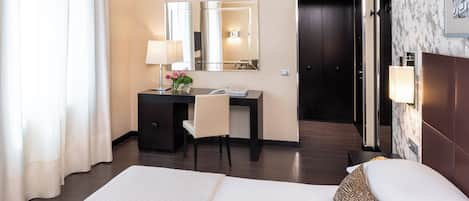A hotel room with a bed, a desk, a chair, a mirror, and a door.