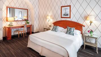 Una habitación de hotel con una cama grande, un escritorio de madera, una silla, un espejo y dos mesitas de noche con lámparas.