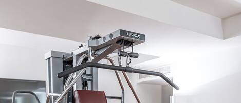 A gym with a weight machine, a treadmill, and a shelf with water bottles and a fruit basket.