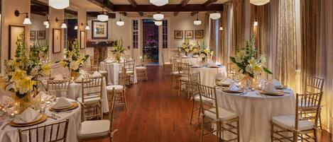 A formal dining room with multiple round tables, each set with white tablecloths, gold-rimmed plates, and gold chairs.