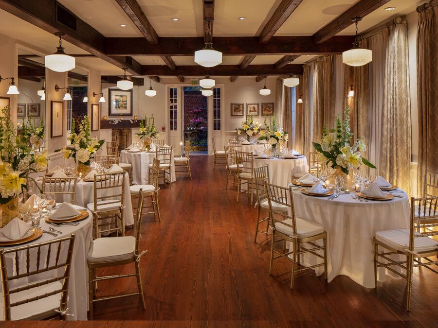 A formal dining room with multiple round tables, each set with white tablecloths, gold-rimmed plates, and gold chairs.