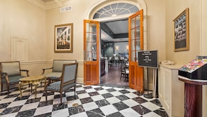 A lobby with a checkered floor, wooden chairs, a reception desk, and a sign indicating the bar is open. - Hotel Provincial (New Orleans)