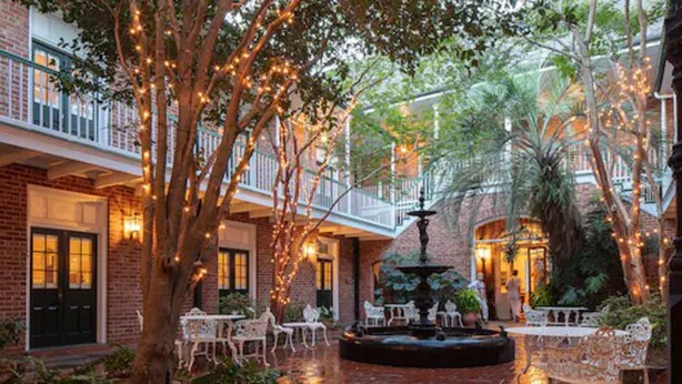 An indoor courtyard with brick walls, white wicker furniture, and a central fountain. - Hotel Provincial (New Orleans)