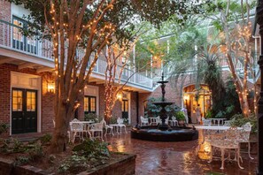An indoor courtyard with brick walls, white wicker furniture, and a central fountain. - Hotel Provincial (New Orleans)
