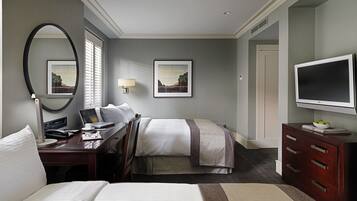 A hotel room with two beds, a desk with a computer, a TV, and artwork on the walls.