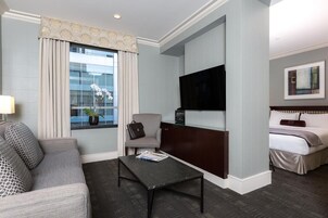 Quarto de hotel com sofá, poltrona, televisão e cama.