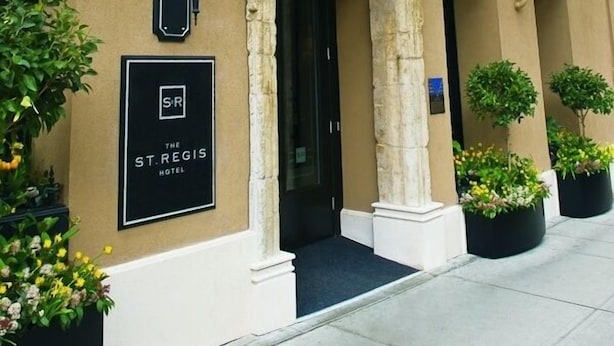 The St. Regis Hotel entrance with a stone archway, a black signboard, and potted plants.