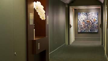 Un pasillo con una puerta de madera, una lámpara floral blanca y un cuadro abstracto colorido en la pared.