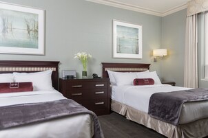 A hotel room with two beds, a nightstand, a dresser, and artwork on the walls.