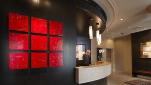 A hotel reception area with a modern design, featuring a black wall with red panels, a curved reception desk, and pendant lighting.