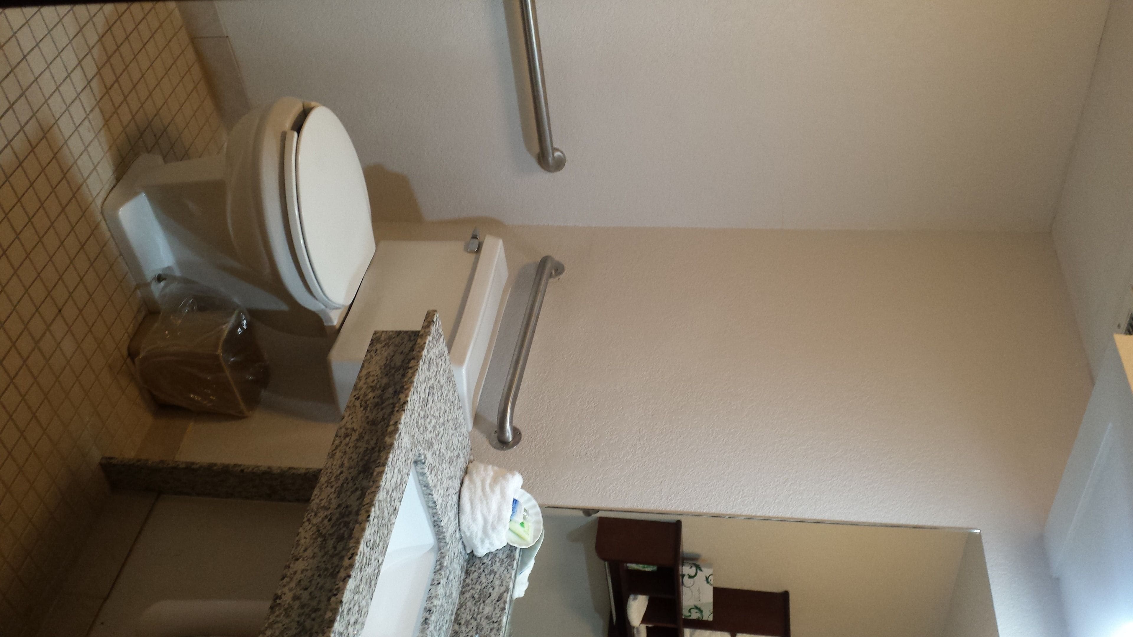 A bathroom with a toilet, grab bars, a towel dispenser, and a trash bin.