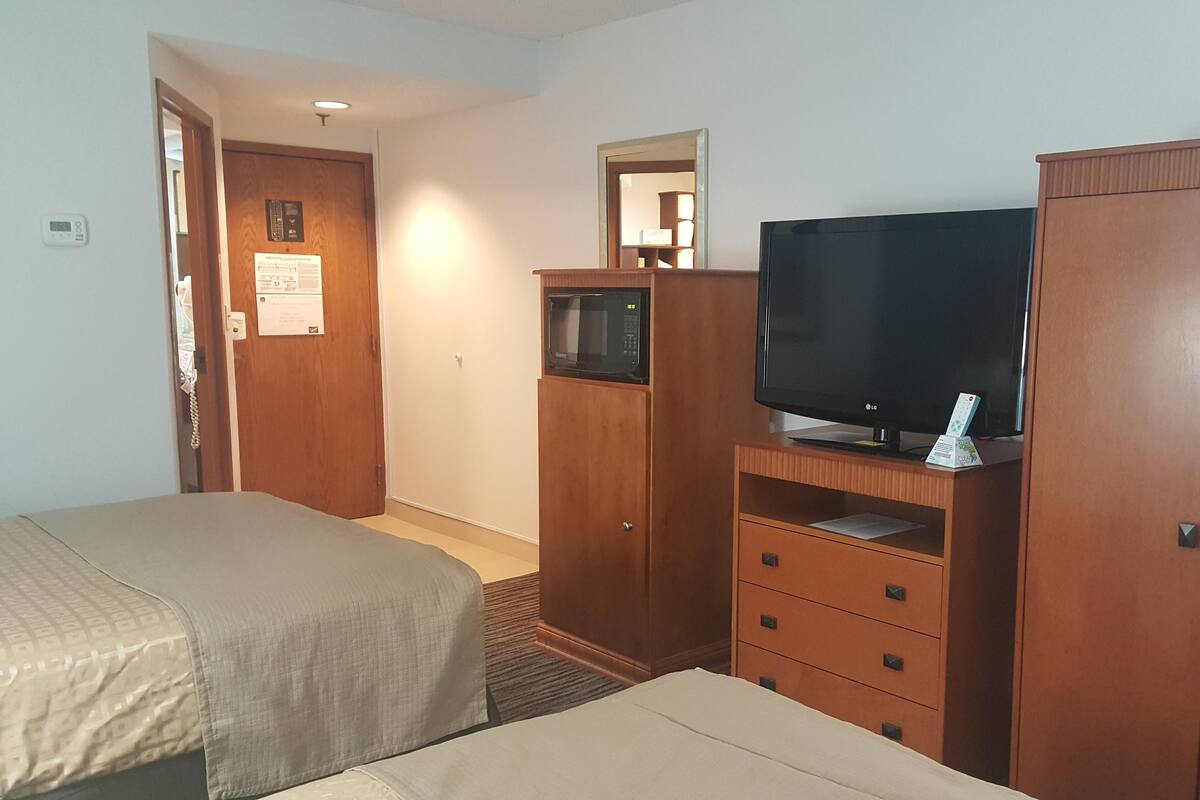 Quarto de hotel com duas camas, televisão, micro-ondas e guarda-roupa.