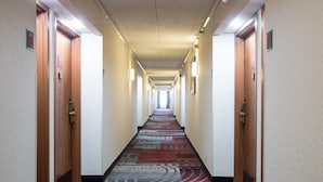 Un corridoio d'albergo con pavimenti in moquette, porte in legno e lampade lungo il soffitto.